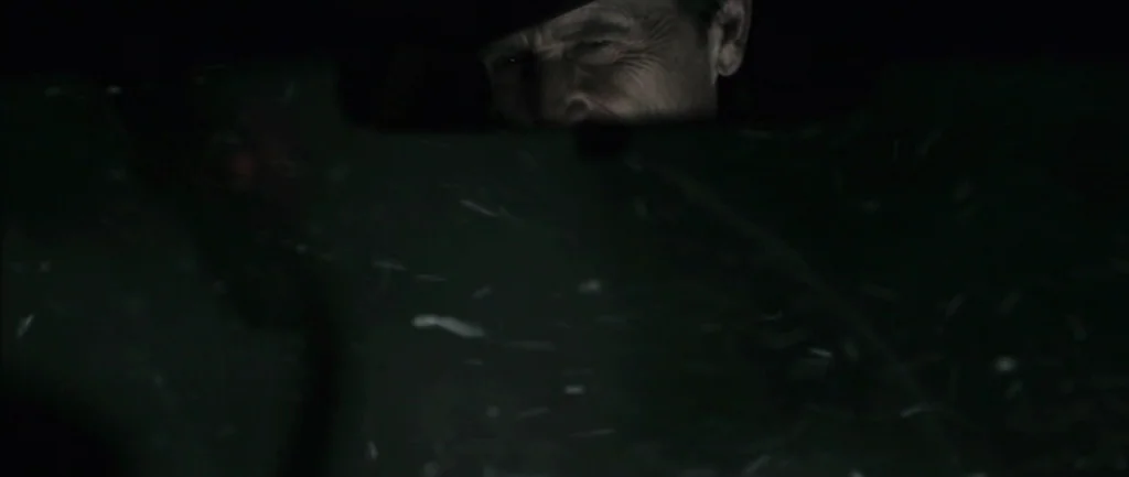 Pontypool (2008) movie still: closeup — The interior of a vehicle at night with a dark windshield surface. An elderly man stares through the glass…