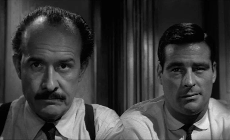 12 Angry Men (1957) movie still: medium — Two men sit side by side in an office with vertical wooden paneling behind them. They stare forward at the…
