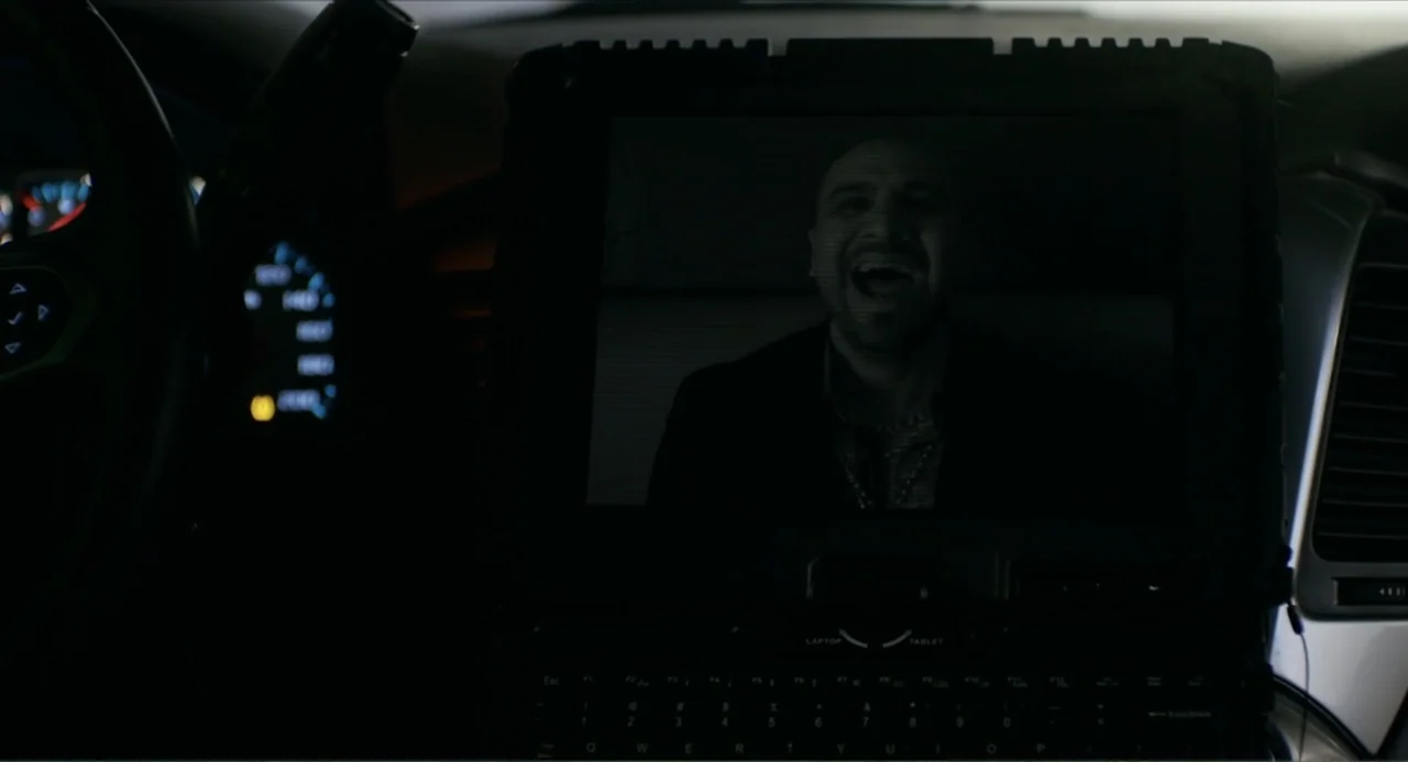 Instantes Capturados (2022) movie still: medium — The interior of a dark car features a laptop screen displaying a video call. A man on the screen…