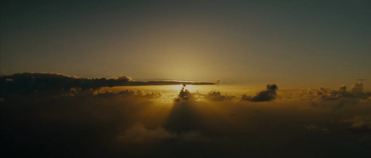 Unbroken (2014) movie still: establishing — A golden sunset sky filled with dense clouds obscures the horizon line. Several small airplanes fly in…