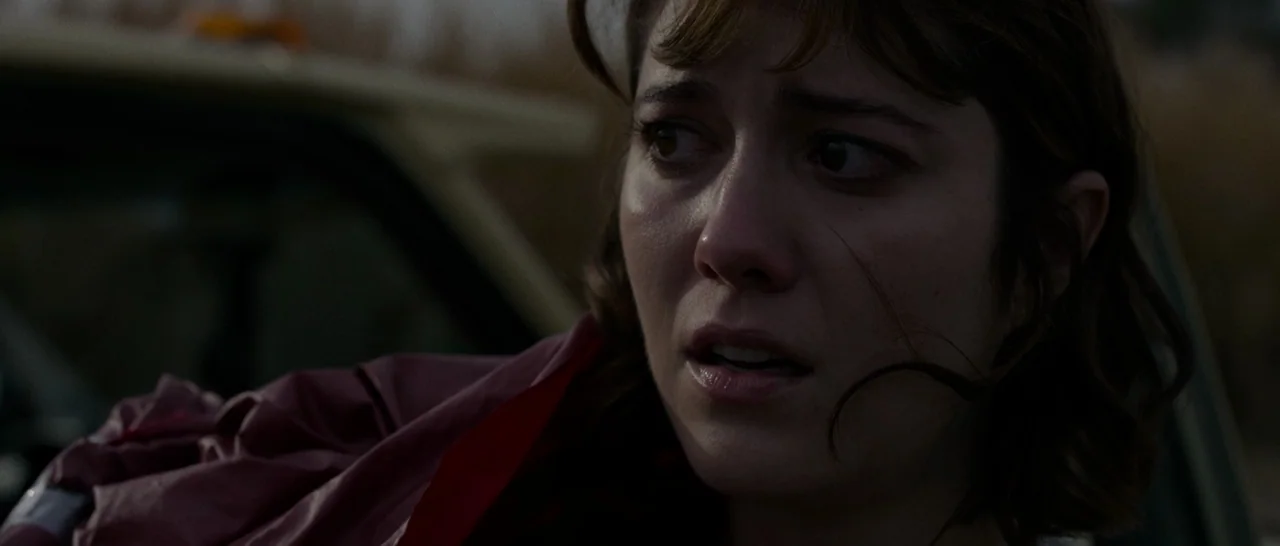 10 Cloverfield Lane (2016) movie still: closeup — A woman sits inside a car with a blurry, grassy field visible outside the window. She directs her…