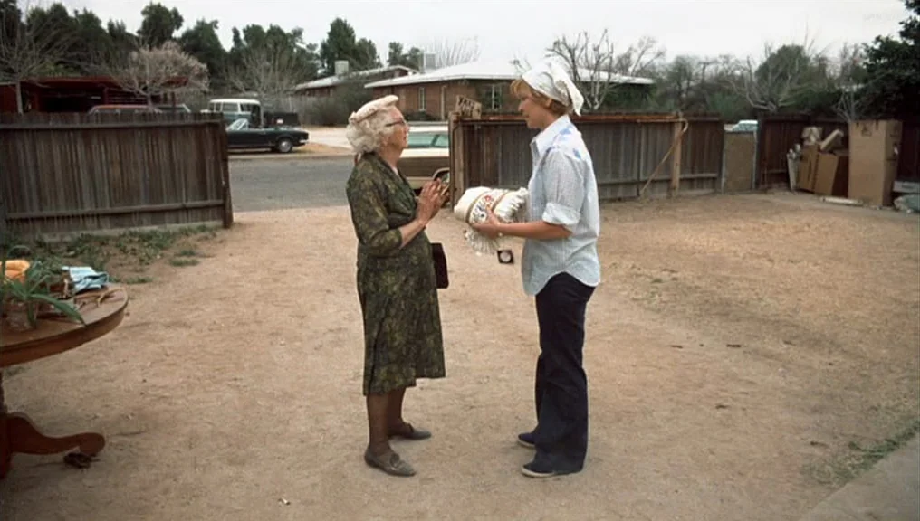 Alice Doesn’t Live Here Anymore (1974) movie still: fullbody — A dirt-covered lot in a suburban area with wooden fencing and parked cars visible.…