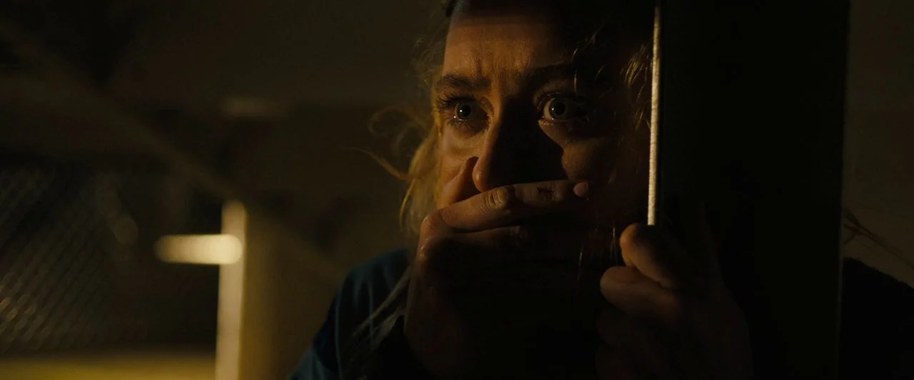 Freaky (2020) movie still: closeup — A dark space with a vertical edge of a wall obstructing part of the view. A woman with blonde hair holds her…