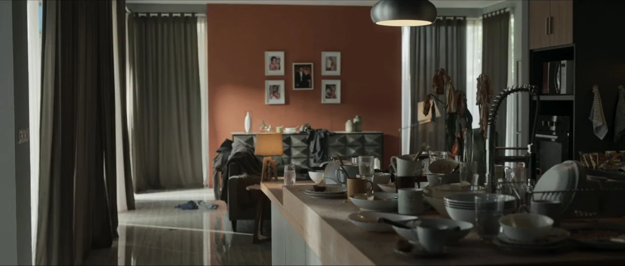 Innocent Vengeance (2023) movie still: wide — A modern open plan kitchen features a cluttered wooden island filled with dirty dishware. A terracotta…