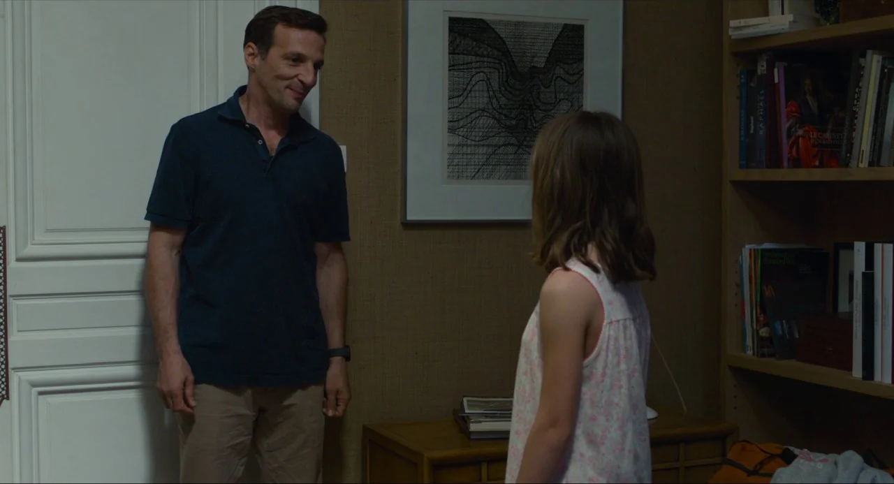 Happy End (2017) movie still: medium — A study features a wooden bookshelf with numerous books and a framed black-and-white print. A man in a dark…