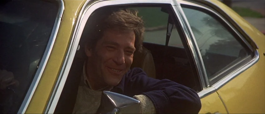 California Split (1974) movie still: medium — A man sits inside a yellow car with the driver's side window rolled down. He smiles while resting his…