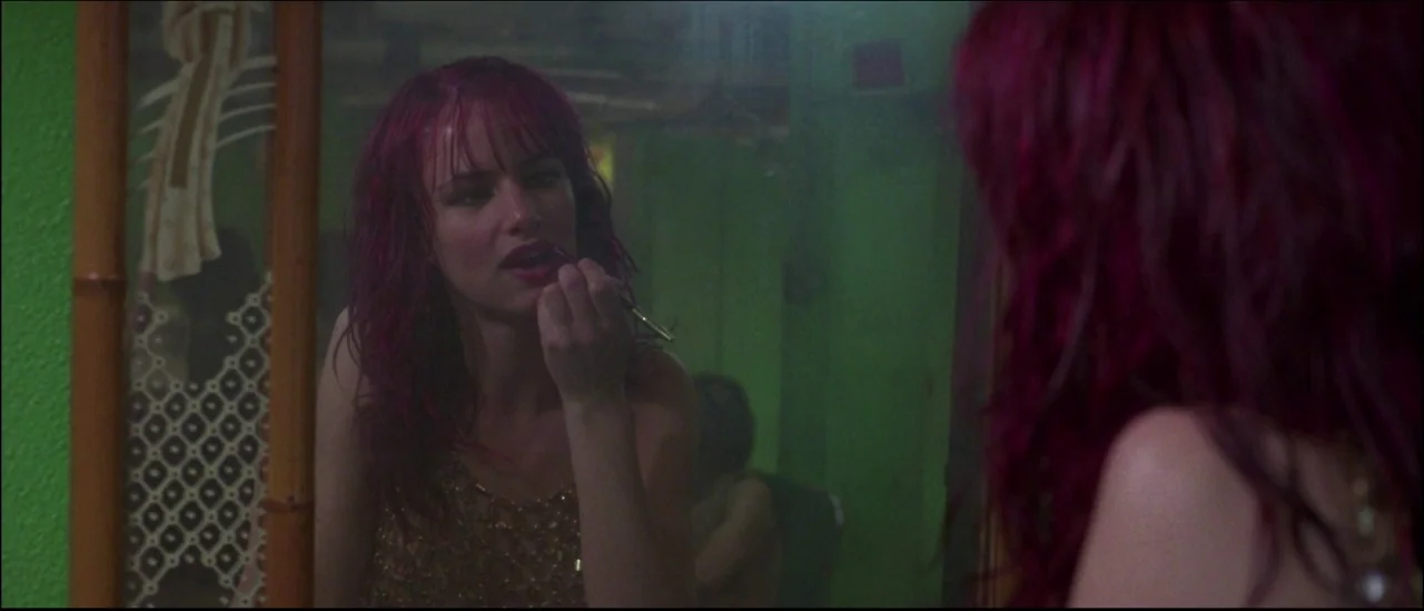 Strange Days (1995) movie still: closeup — A dimly lit room with a bright green wall and bamboo-framed mirror. A young woman with magenta hair…