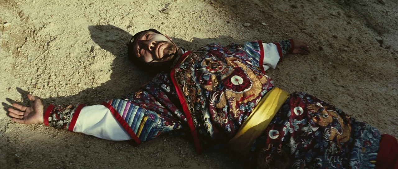 A Touch of Zen (1971) movie still: medium — A man lies motionless on dry, coarse sand under intense direct sunlight. The subject wears a highly…