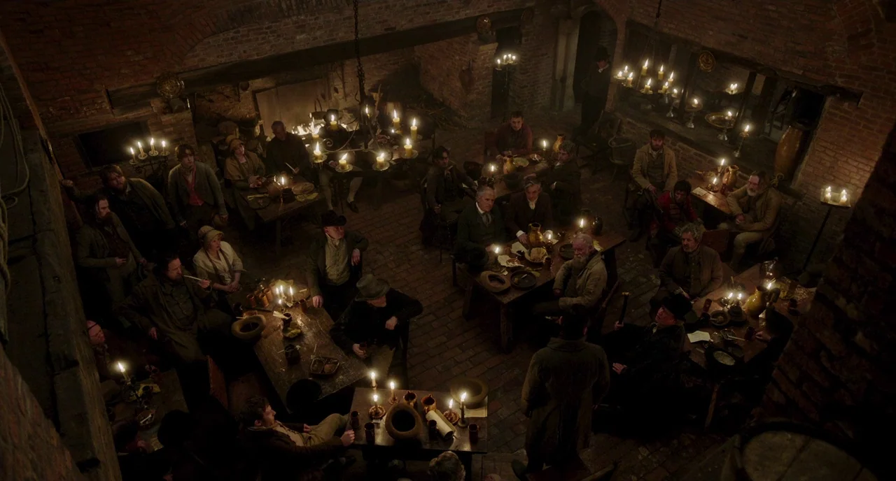 Peterloo (2018) movie still: wide — A subterranean tavern features exposed brick walls, arched brick ceilings, and wooden tables. Numerous people…