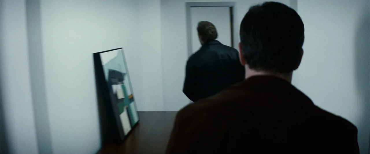 Hereafter (2010) movie still: medium — A minimalist white interior corridor features a piece of abstract art leaned against the wall. Two men walk…