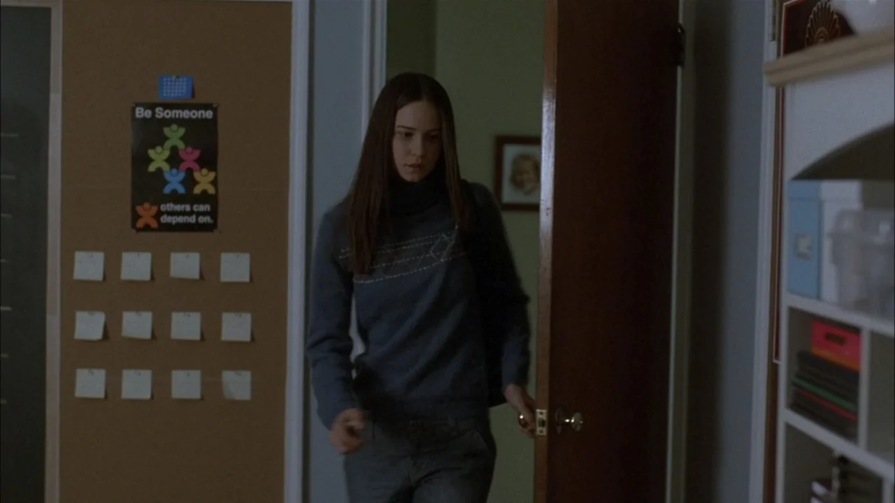 The Babysitters (2008) movie still: medium — A residential hallway with a cork message board featuring notes and a poster on the wall. A young woman…