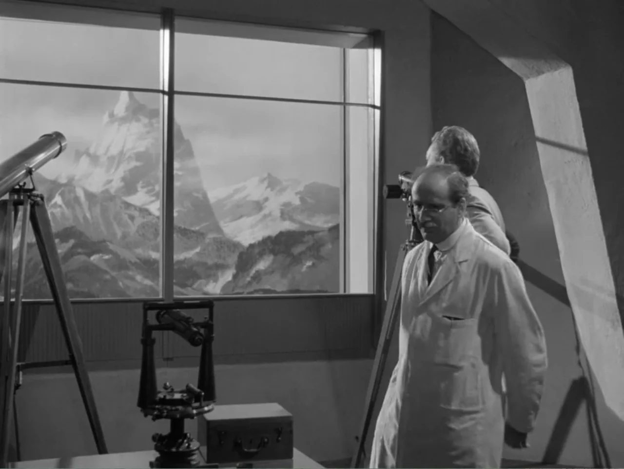 The Crawling Eye (1958) movie still: medium — An interior observatory room contains scientific equipment and a large window showing mountain peaks.…