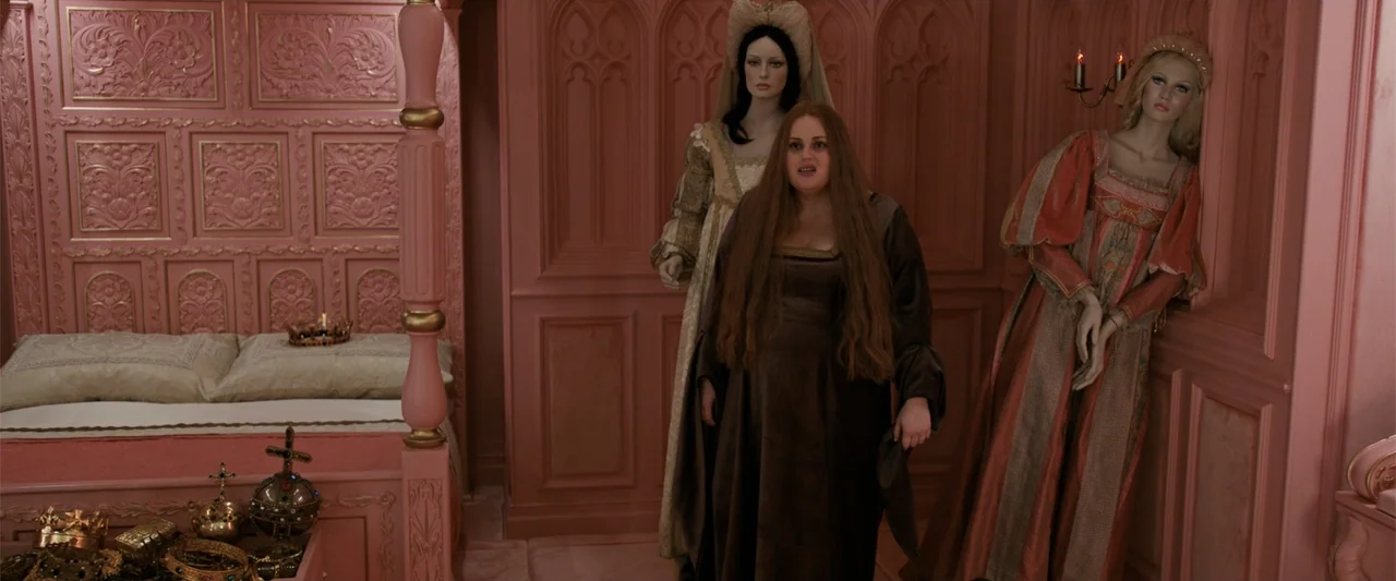 The Hustle (2019) movie still: medium — A pink-toned renaissance bedchamber features intricate woodwork and a four-poster canopy bed. A woman stands…