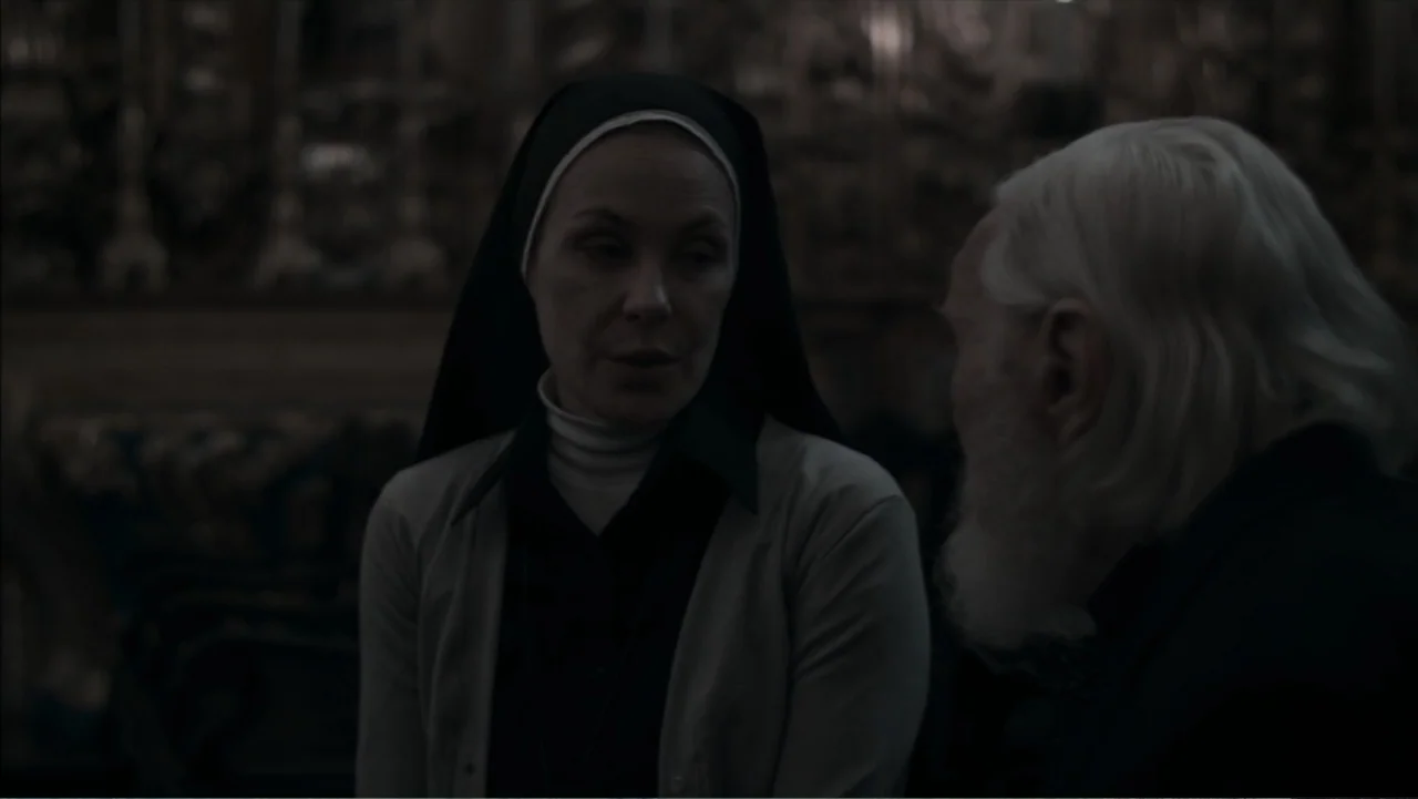 The Grotto (2022) movie still: medium — A dimly lit indoor space featuring ornate, blurred architectural details in the background. A nun in a habit…