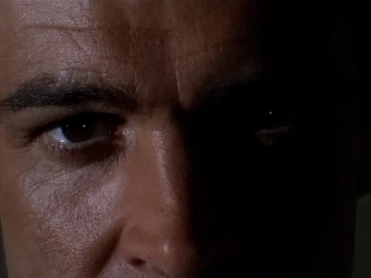 Marnie (1964) movie still: closeup — A dark indoor space where a man's face is partially obscured by heavy shadows. He stares forward directly at…
