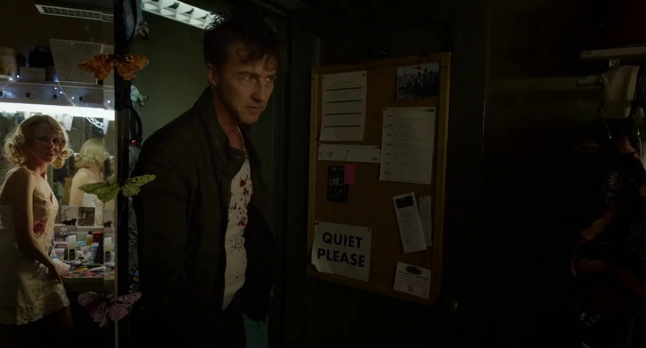 Birdman (2014) movie still: medium — An interior space features a dark doorway with a bulletin board marked 104D. A blood-stained man stands in the…