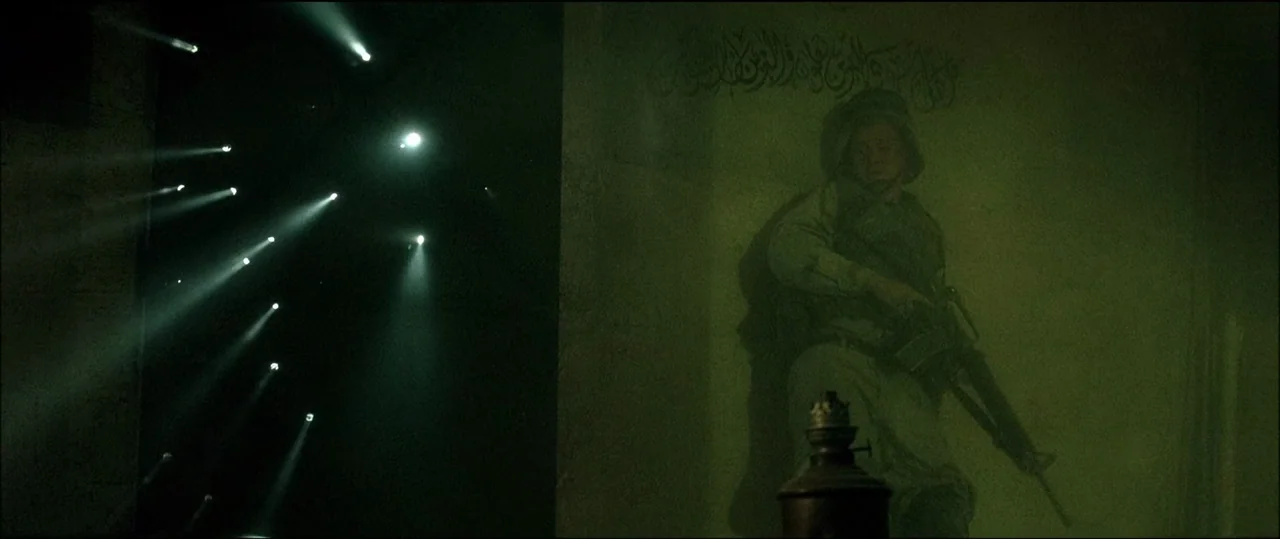 Black Hawk Down (2001) movie still: wide — A dark indoor space features a wall with a large painted mural of a soldier. Several beams of light cut…