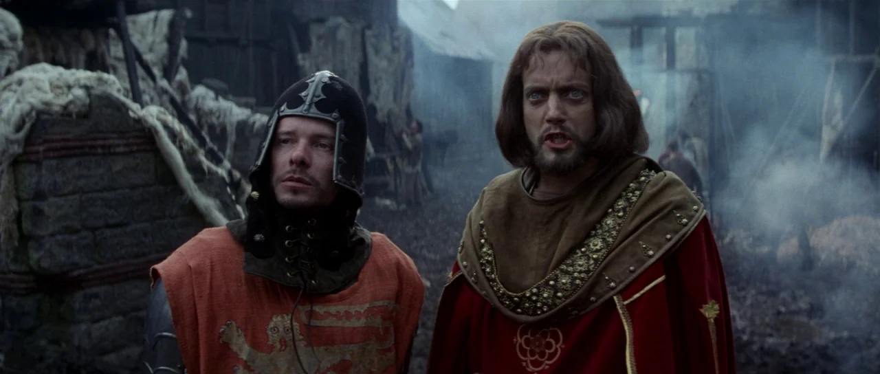 Braveheart (1995) movie still: medium — A muddy, smoke-filled medieval site features wooden structures and debris in the background. Two men wearing…