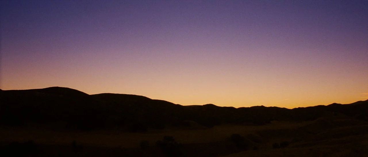 Casa De Mi Padre (2012) movie still: establishing — A dark, silhouetted range of rolling hills sits under a vibrant twilight sky. The horizon glows…