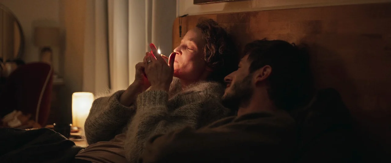 More Than Ever (2022) movie still: medium — A dimly lit bedroom featuring a wooden headboard and a soft glowing table lamp. A woman lights a…