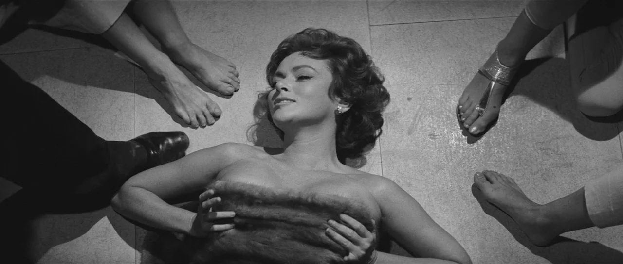 La Dolce Vita (1960) movie still: medium — A woman lies on a hard floor surrounded by the feet of several standing individuals. She is partially…