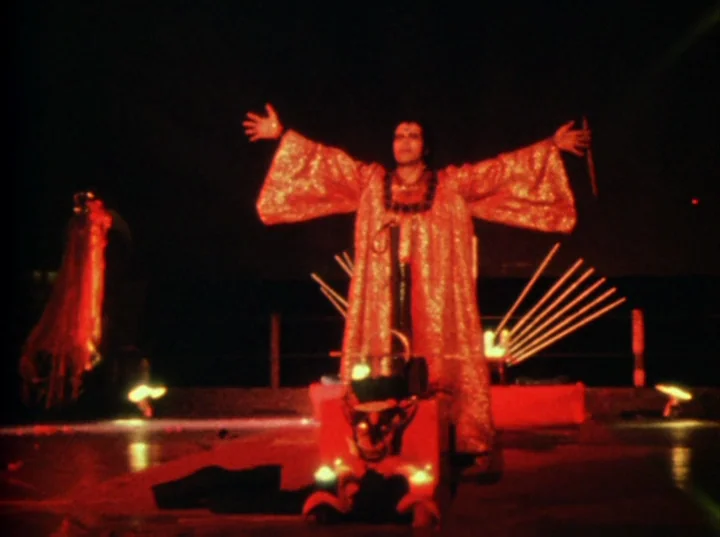 Invocation of My Demon Brother (1969) movie still: fullbody — A dark stage features an altar with a carved demon face and flickering candles. A man…