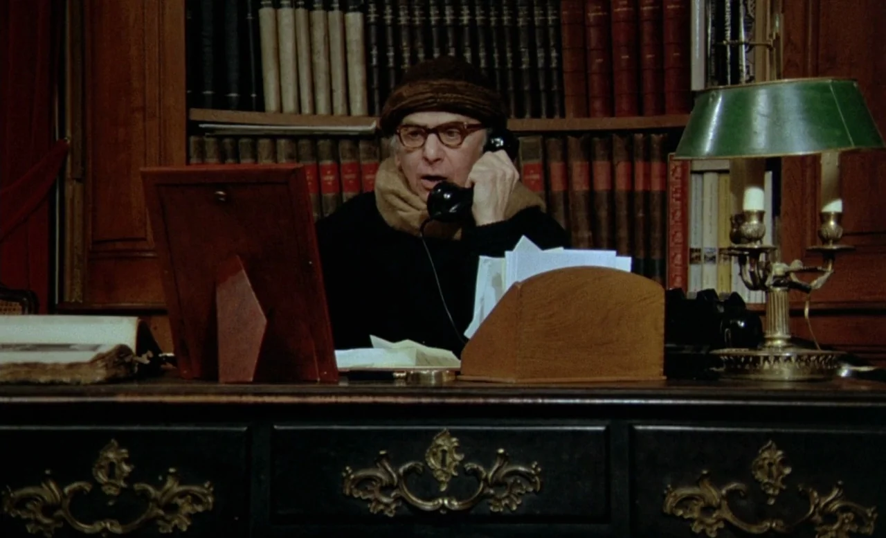The Beast (1975) movie still: medium — A wood-paneled room contains floor-to-ceiling bookshelves and a large ornate dark-wood desk. An elderly man…