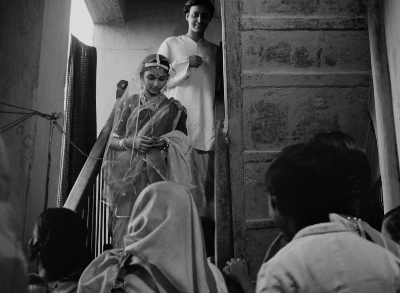 Apur Sansar (1959) movie still: medium — A narrow stone staircase inside an old building with peeling walls. A young woman in a sari walks down…