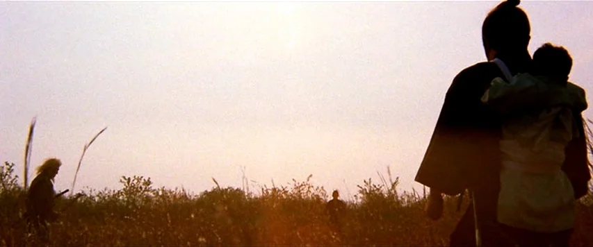 Lone Wolf and Cub: Sword of Vengeance (1972) movie still: wide — An open grassy field under a bright, washed-out sky at sunset. A man carrying a…