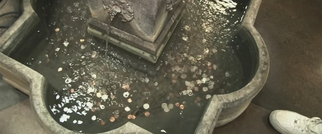 Giannis: The Marvelous Journey (2024) movie still: medium — A stone basin features a central fountain spraying water over collected coins. A…