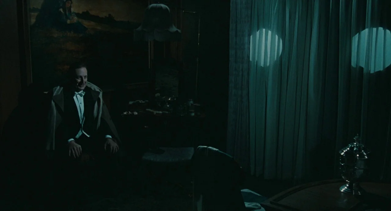 And The Ship Sails On (1983) movie still: medium — A dimly lit, moody hotel room with heavy curtains and traditional furniture. A man in a tuxedo…