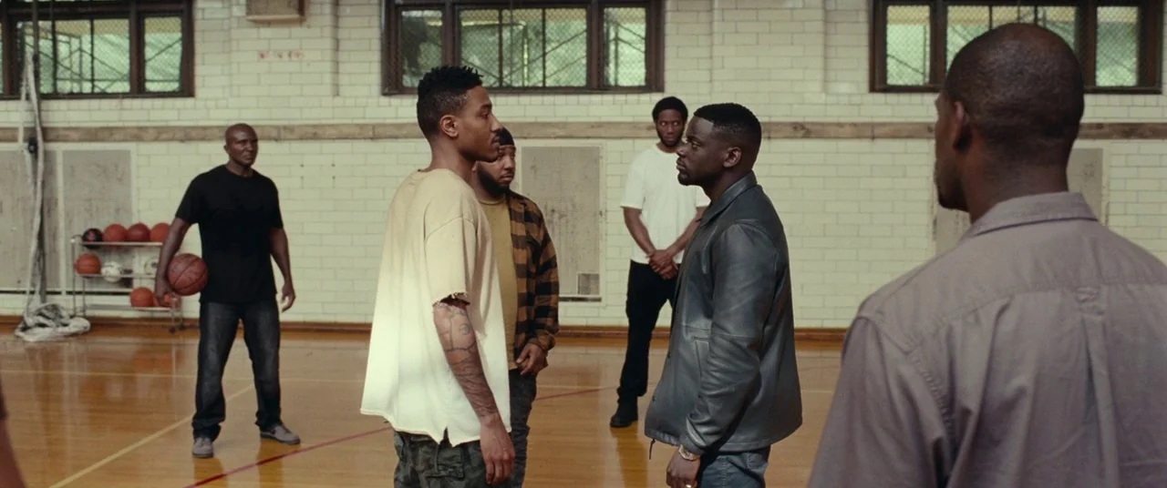 Widows (2018) movie still: fullbody — An indoor basketball court features white tiled walls and a polished wood floor. A small group of men stand…