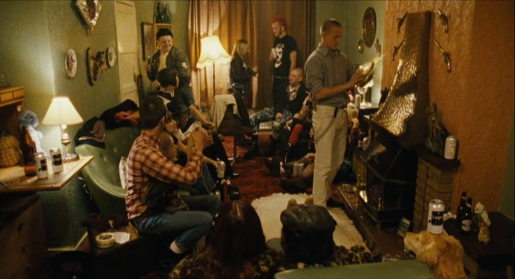 This Is England (2006) movie still: wide — A cluttered 1990s living room features patterned wallpaper and various household ornaments. A group of…
