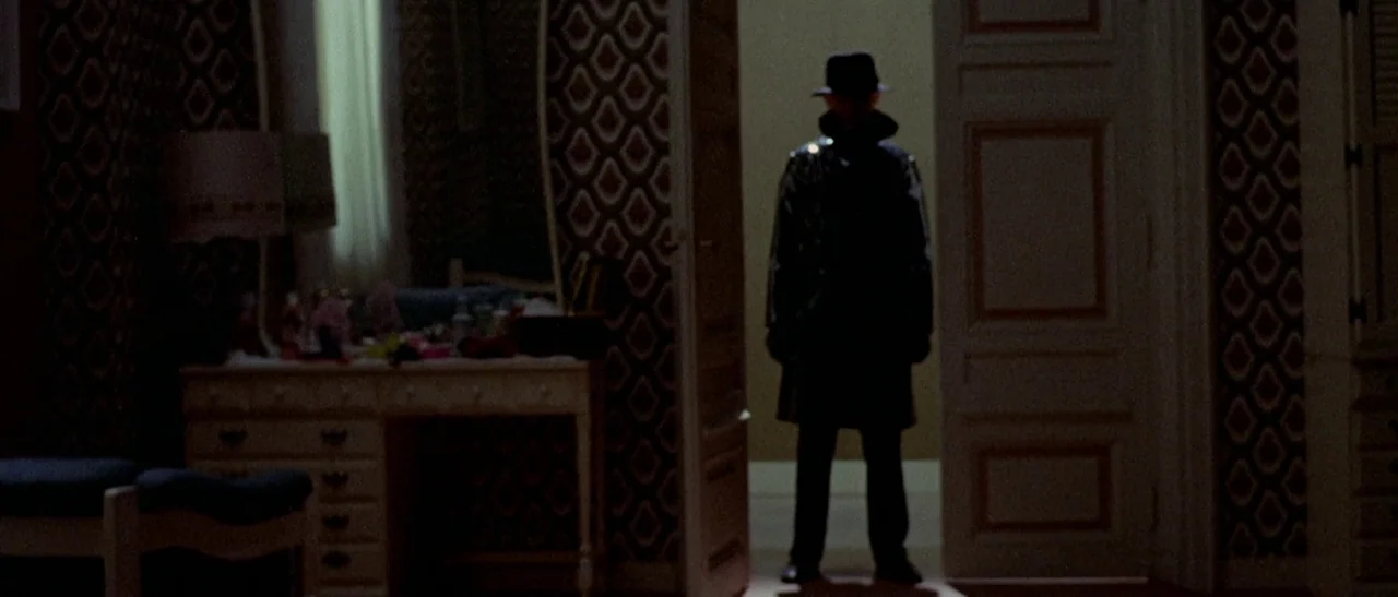 The Bird With The Crystal Plumage (1970) movie still: fullbody — A patterned wallpaper wall features a doorway where a man stands. The figure in the…