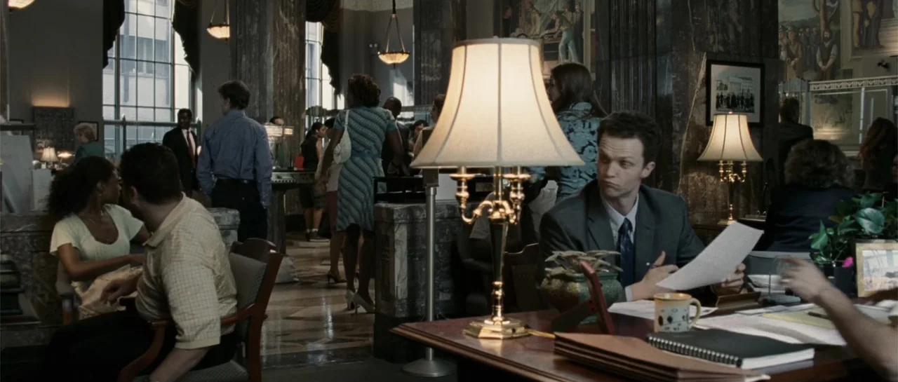 Inside Man (2006) movie still: medium — A bustling bank lobby features dark marble columns and patterned stone floors. A man sits at a desk…