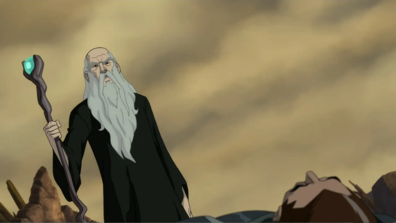 Justice League Dark (2017) movie still: medium — An elderly man in a dark robe stands in a desolate, rocky landscape. The wizard holds a wooden…