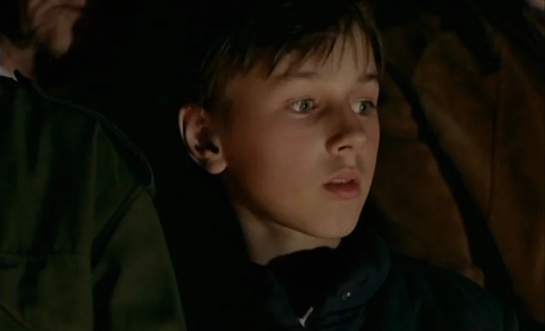 No End (1985) movie still: closeup — A dimly lit interior space is visible behind the subject. A young boy sits looking forward with his mouth…