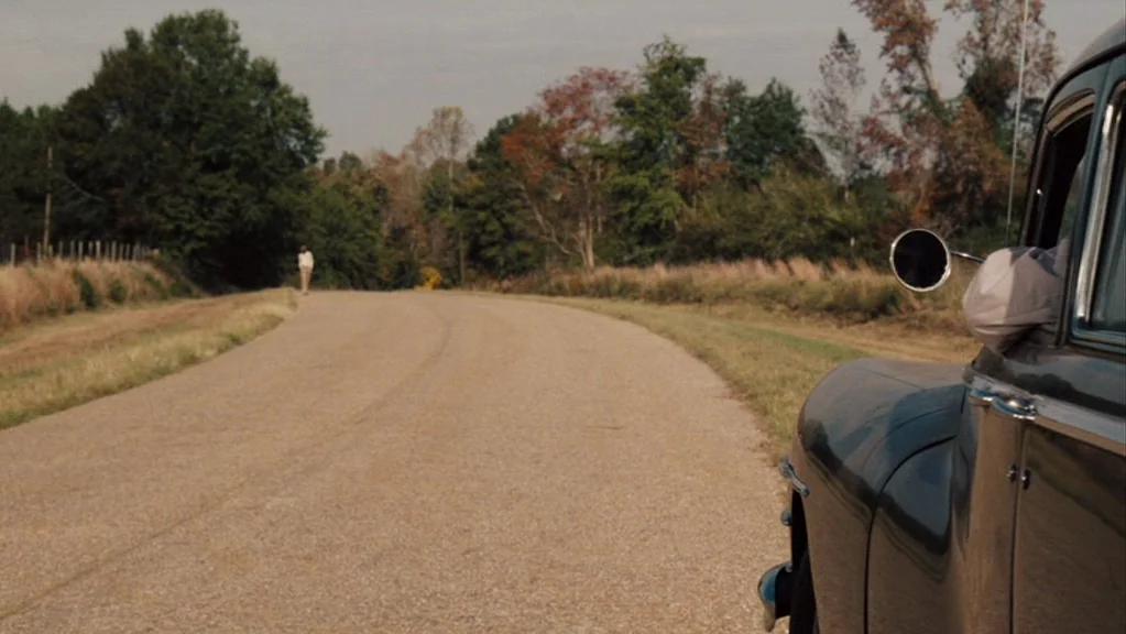 Honeydripper (2007) movie still: wide — A rural asphalt road curves into the distance flanked by grass and autumn trees. A vintage car occupies the…