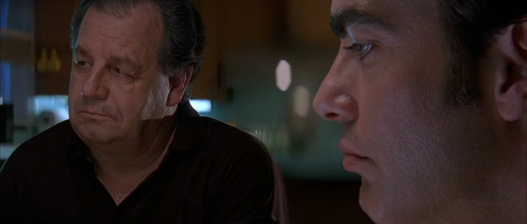 The Underneath (1995) movie still: medium — Two men sit together in a dim, shadowed indoor space at night. The men gaze in similar directions while…