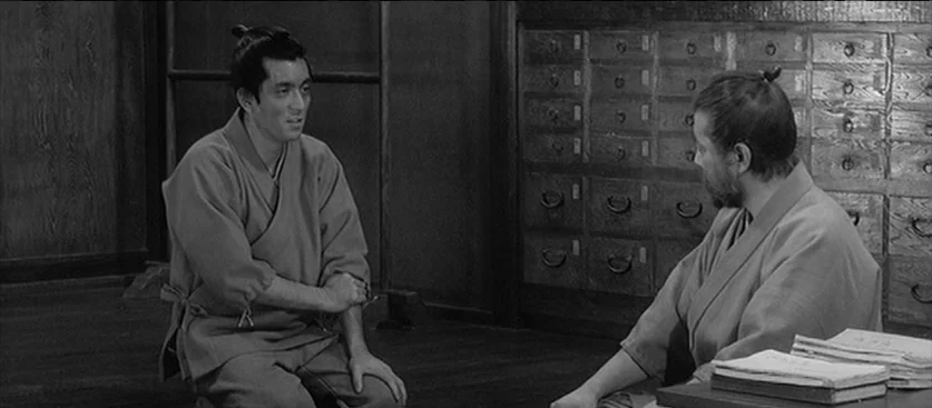 Red Beard (1965) movie still: medium — A traditional Japanese apothecary shop features wooden walls and extensive rows of storage drawers. Two men…
