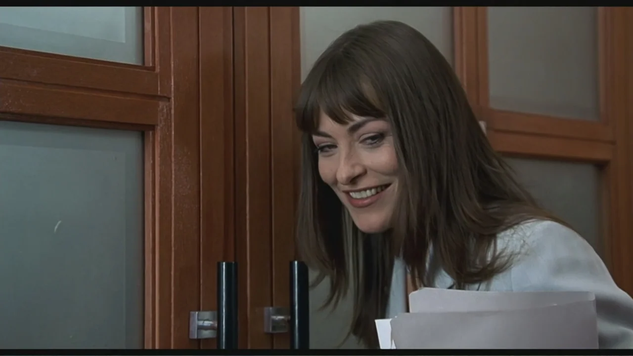 Liar Liar (1997) movie still: medium — An interior hallway features dark wood paneling with inset frosted glass panels. A woman in a light blue…