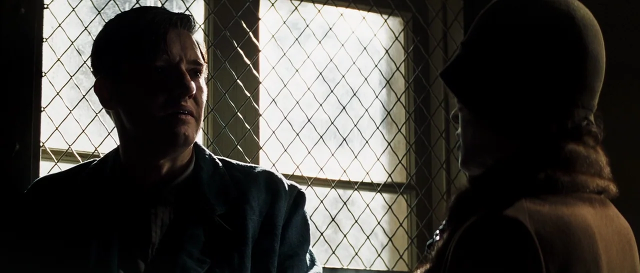 Changeling (2008) movie still: medium — A window with a metal mesh screen illuminates two people sitting across from each other. They talk quietly…