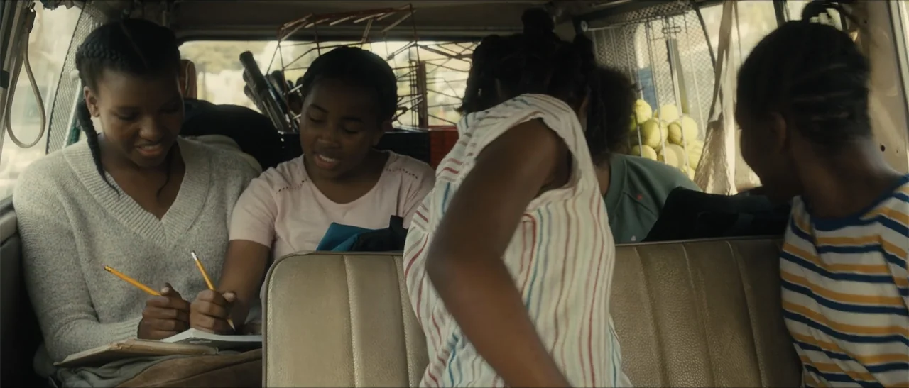 King Richard (2021) movie still: medium — The interior of a van displays several girls occupied with schoolwork and conversation. They sit on beige…
