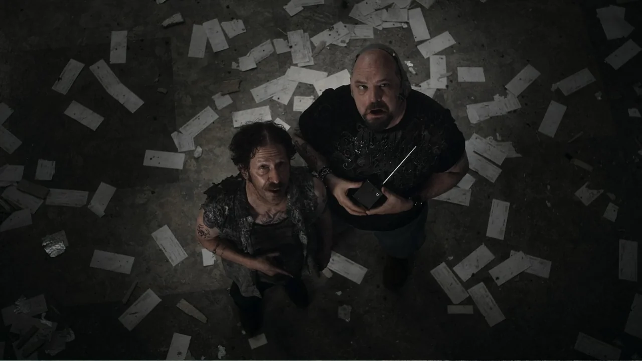 Flypaper (1999) movie still: medium — An interior space with a concrete floor covered in scattered white paper fragments. Two men stand together…