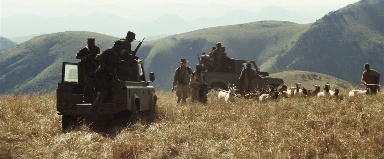 Blood Diamond (2006) movie still: wide — A dry grassy savanna with rolling hills in the background under clear skies. Several armed men in off-road…