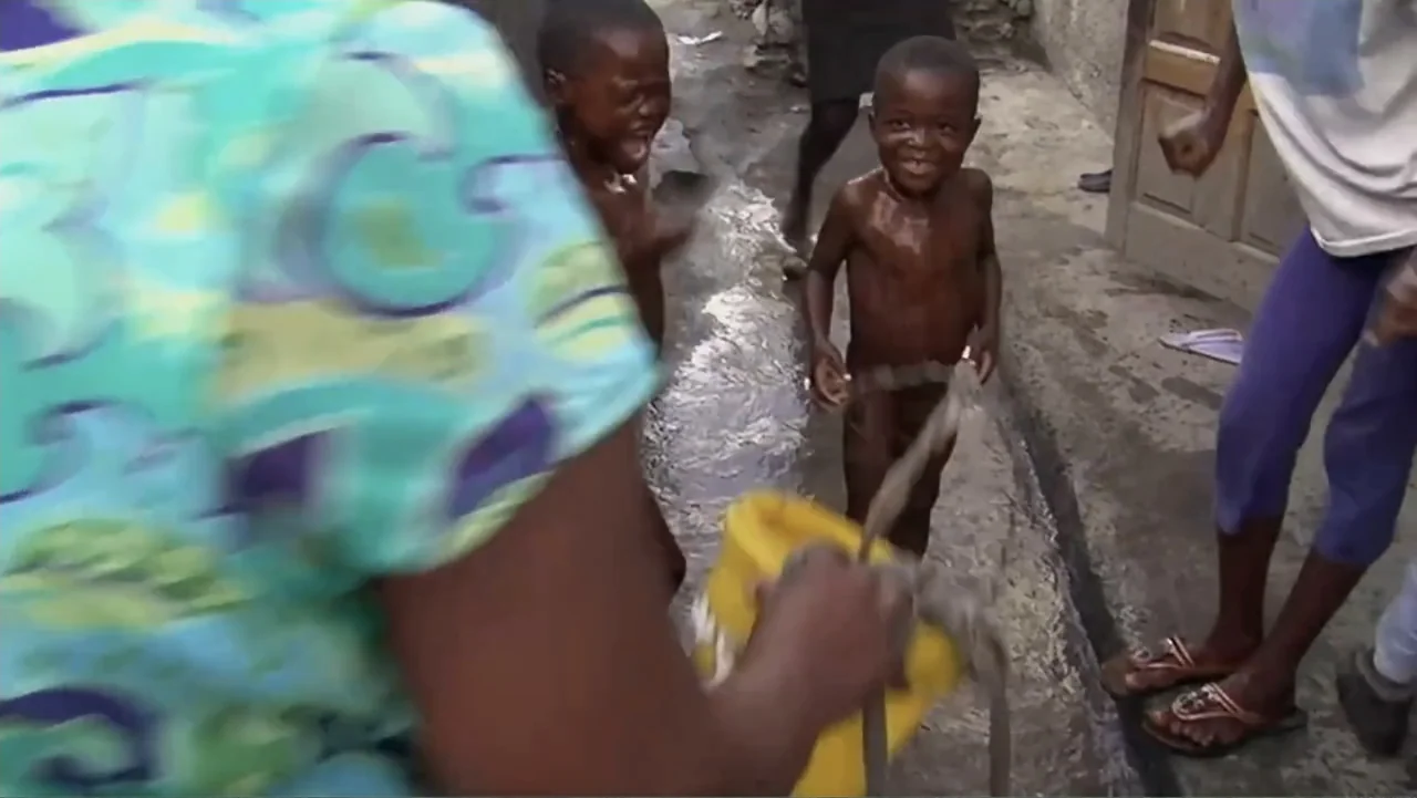 Sister (2014) movie still: medium — A narrow alleyway has wet, uneven pavement and weathered concrete walls. Two young boys stand together near a…