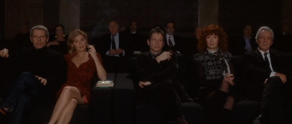 You Ain’t Seen Nothin’ Yet (2012) movie still: medium — A dark, modern movie theater with several rows of seats occupied by individuals. The people…