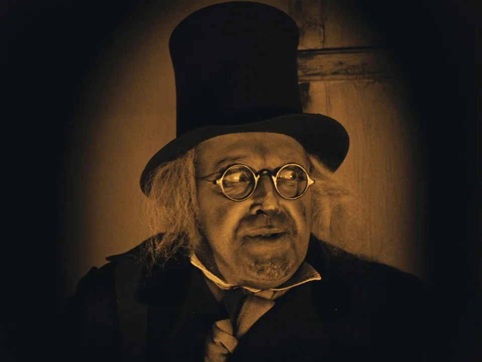 The Cabinet of Dr. Caligari (1920) movie still: closeup — A dimly lit indoor setting features a person in historical period clothing. An elderly man…
