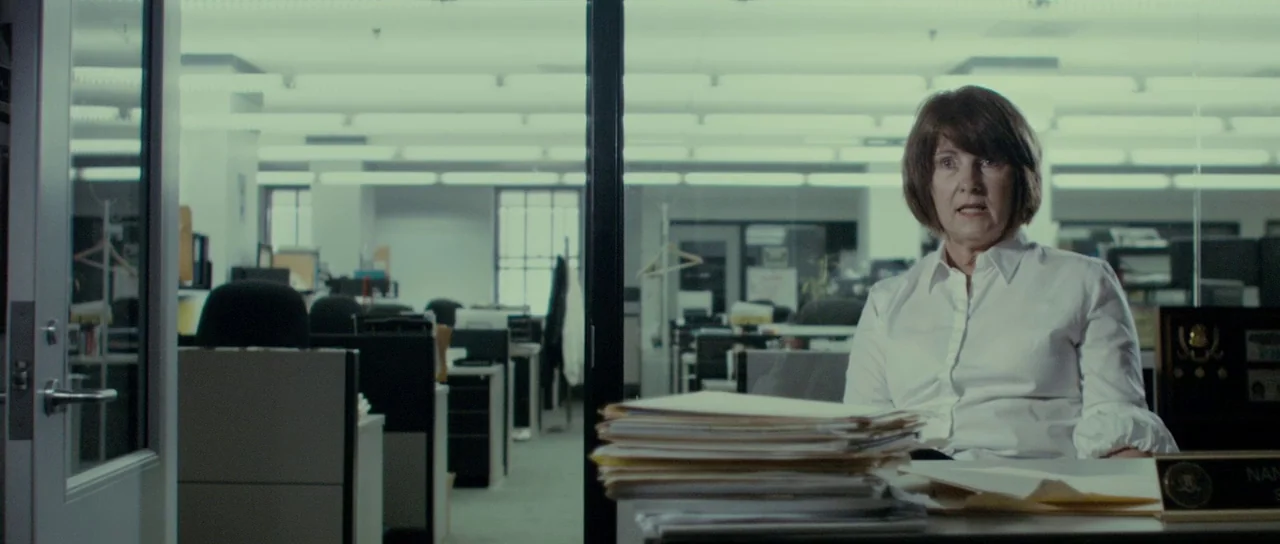 The Imposter (2012) movie still: medium — A sterile corporate office with cubicles and glass partitions under bright overhead lighting. A…