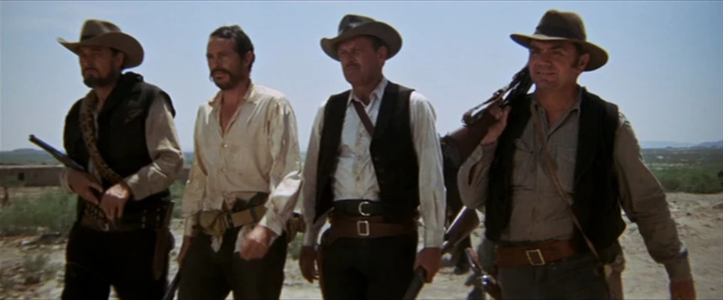 The Wild Bunch (1969) movie still: fullbody — Four men in western attire walk across a arid, open desert landscape. They carry rifles and wear gun…